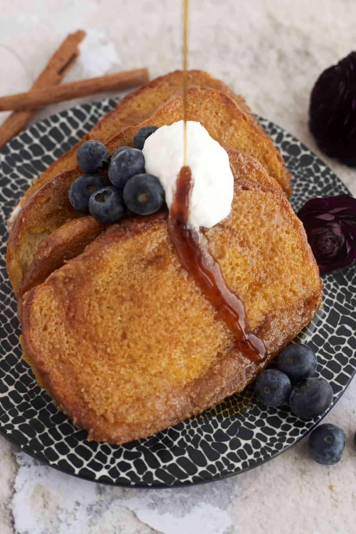 a plate of easy french toast with caramel sauce, whipped cream, and blueberries with syrup being poured on top