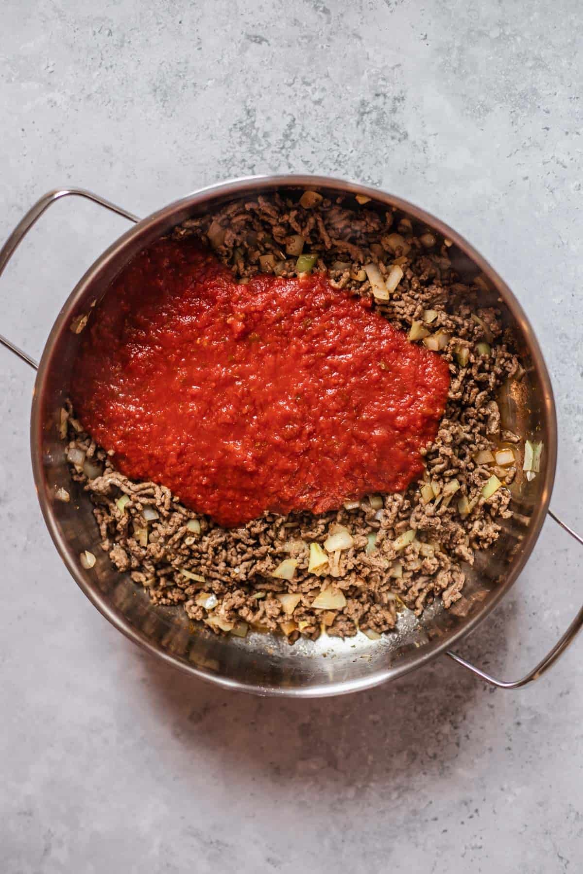 beef, onions, and spices in a large pot topped with tomato sauce