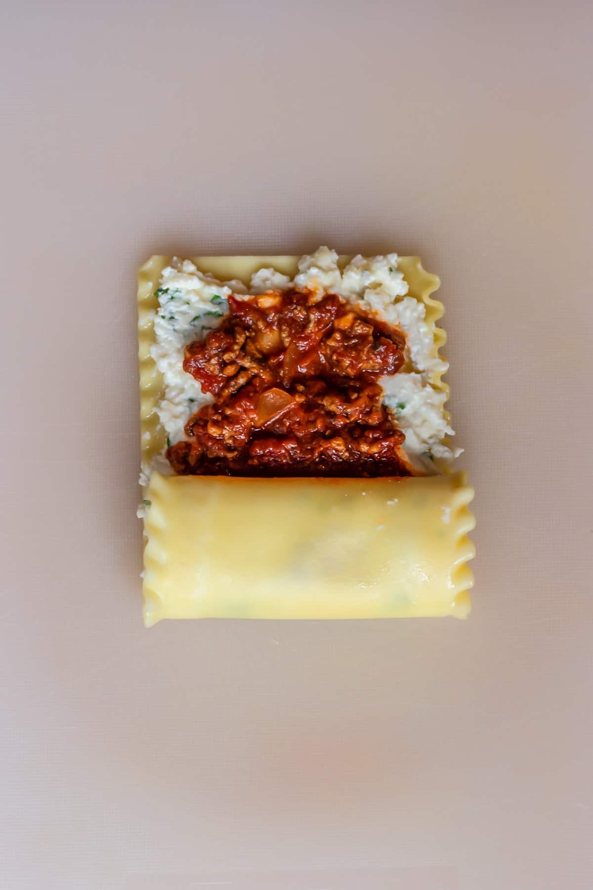 a lasagna noodle layered with ricotta cheese and beef marinara sauce halfway rolled