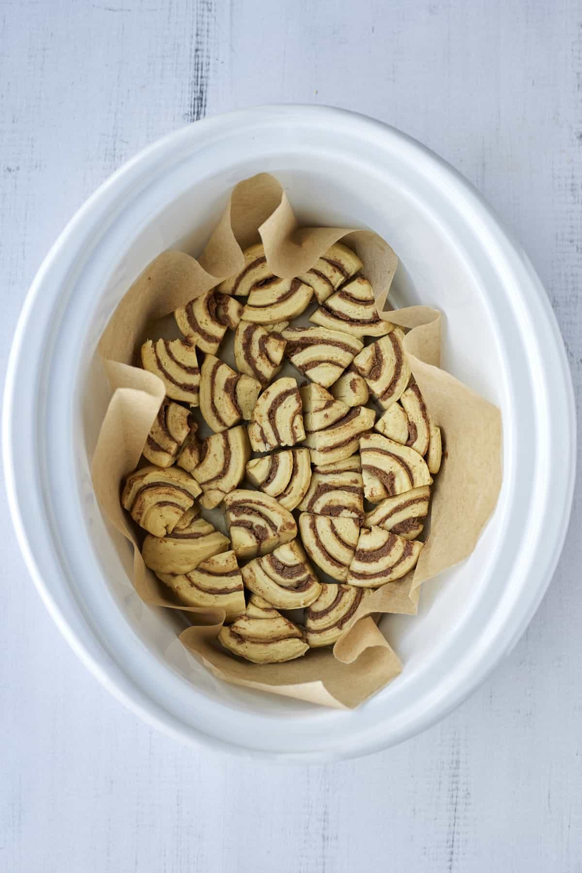 pieces of cinnamon roll dough in the bottom of a parchment lined slow cooker.