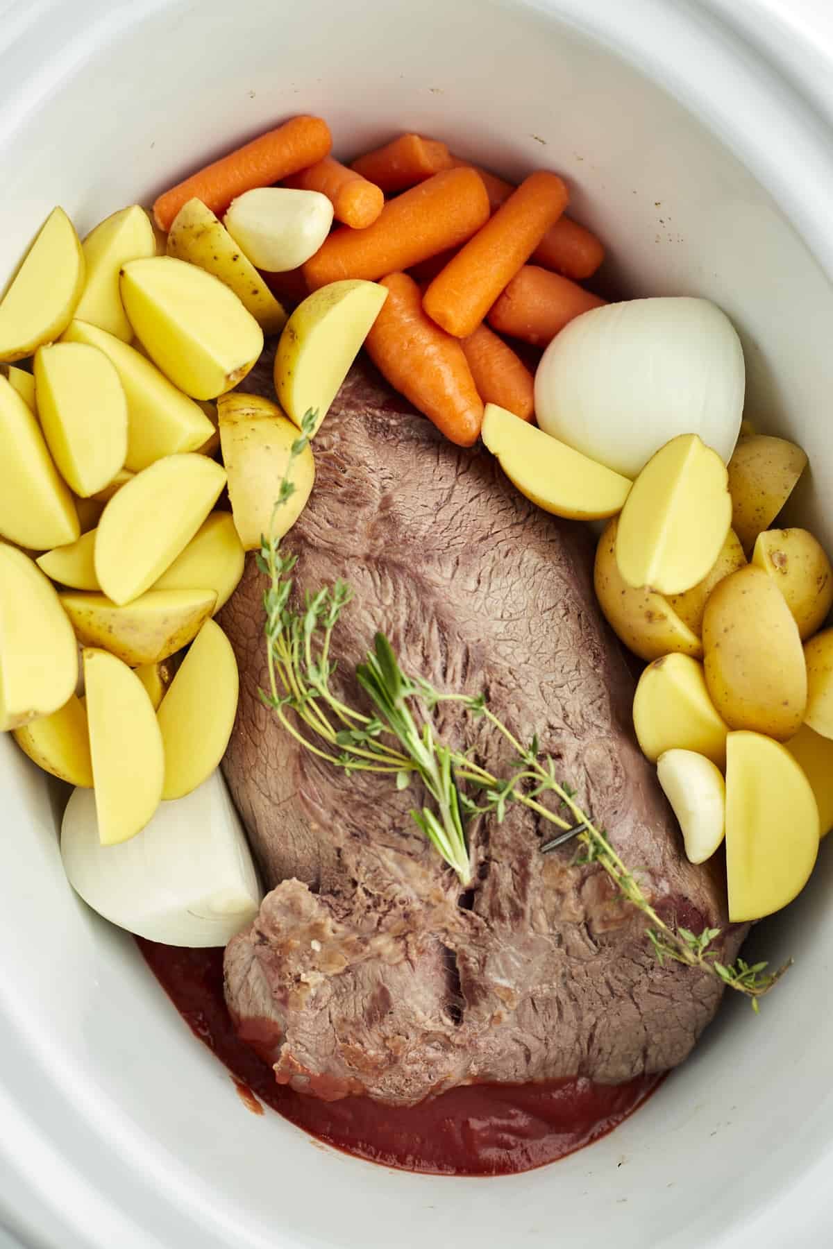beef pot roast, golden potatoes, carrots, onions, and herbs in a slow cooker.