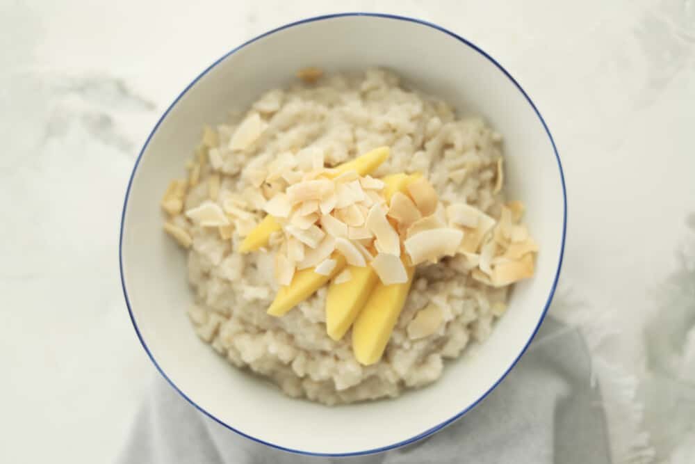 a bowl of slow cooker coconut sticky rice topped with sliced mangoes and coconut flakes