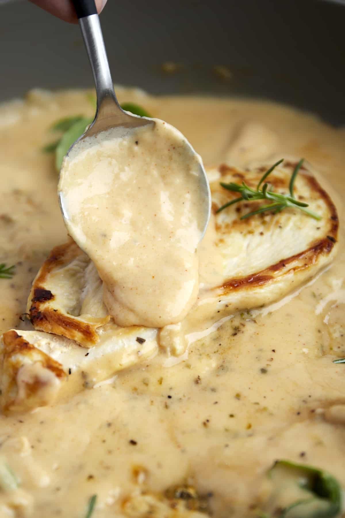 creamy parmesan sauce being spooned over a cooked chicken breast in a skillet