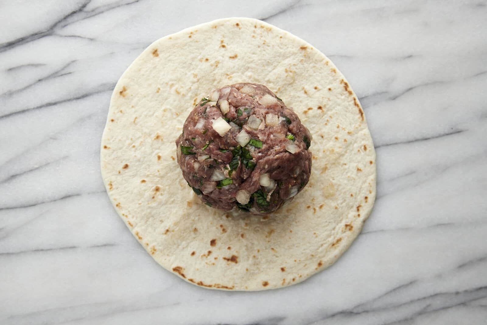 Seasoned ground beef patty on top of a tortilla.
