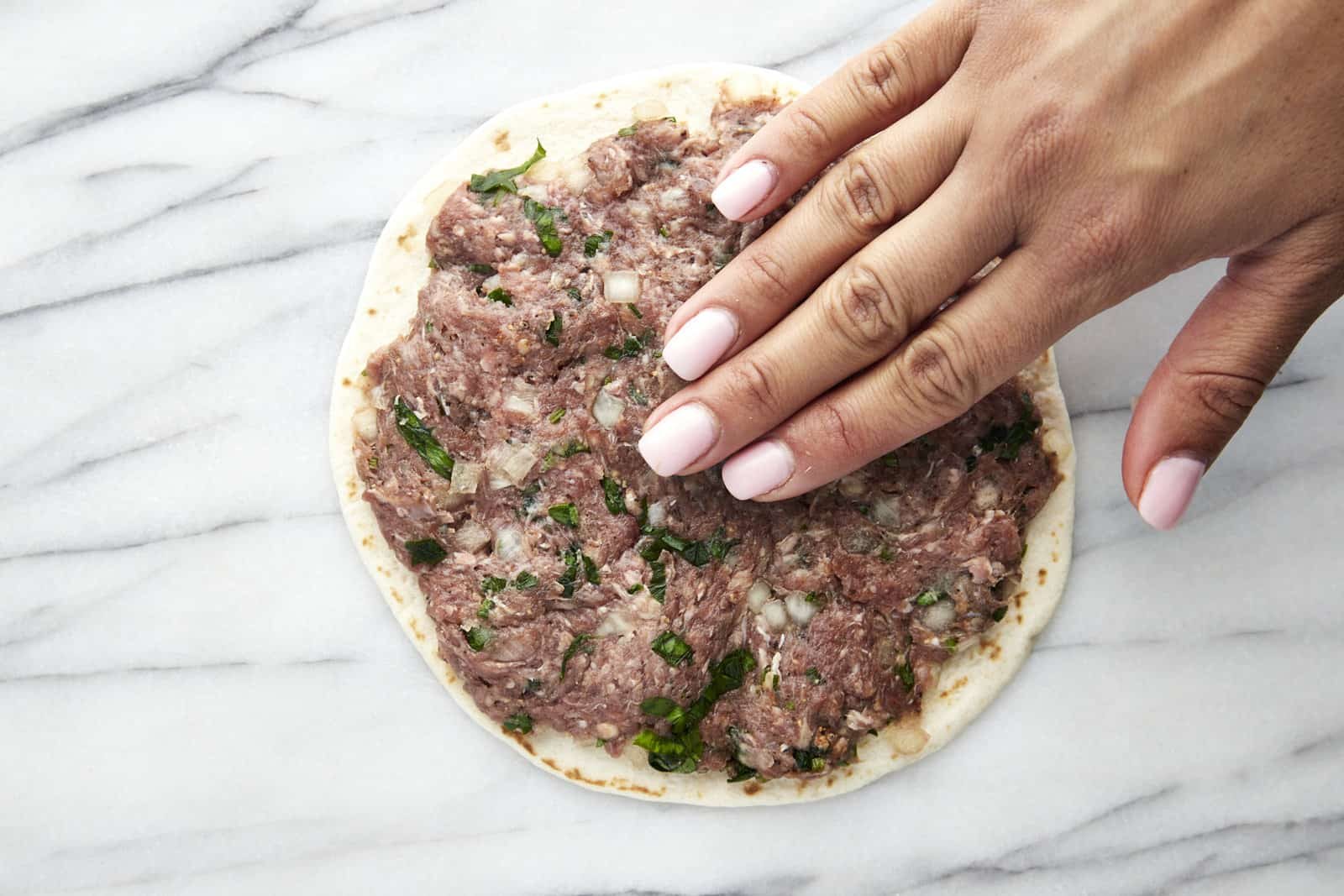 A hand smashing seasoned ground beef onto a tortilla.