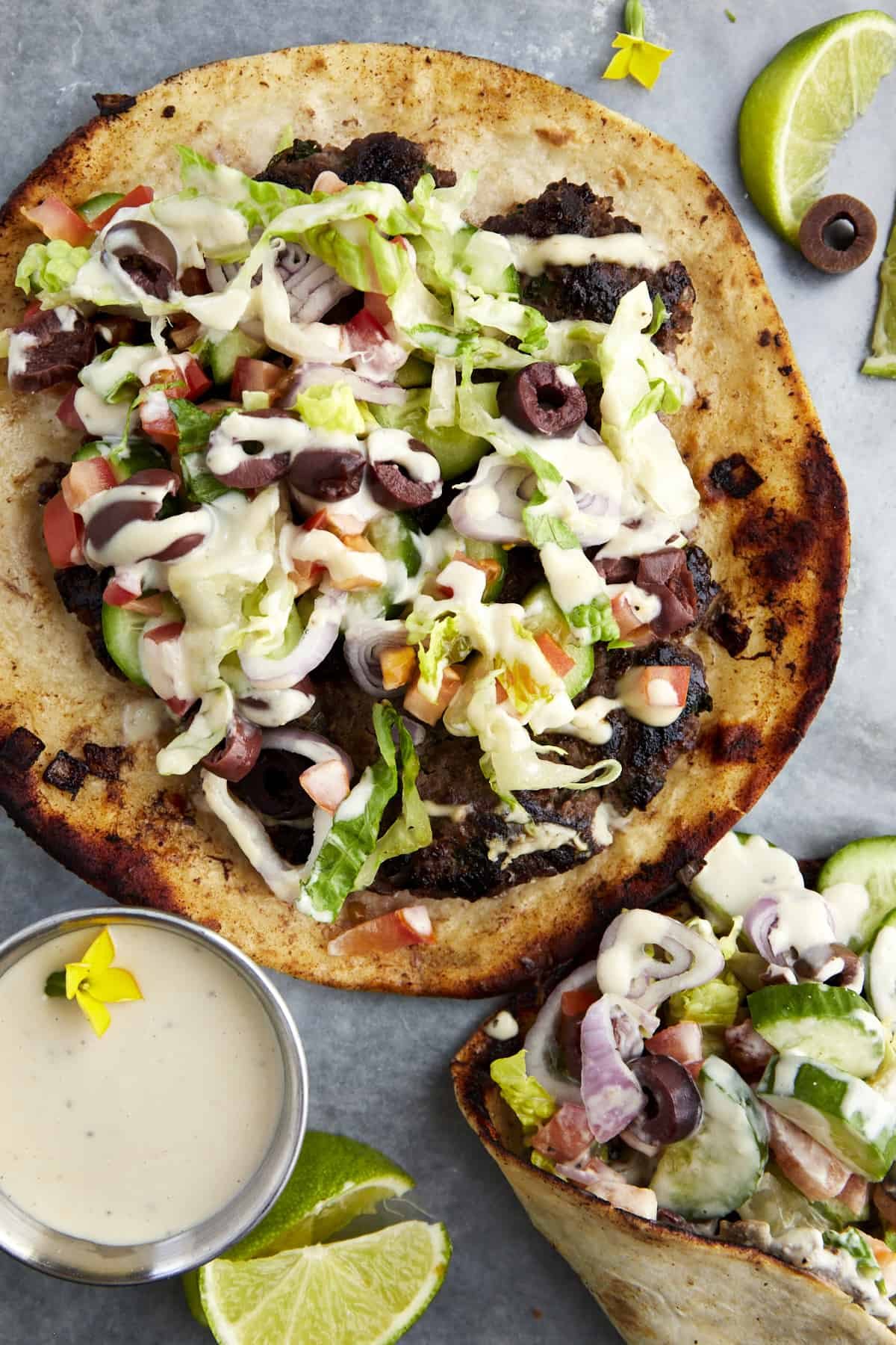 Greek-inspired smashed taco topped with lettuce, onion, tomatoes, olives, and tahini.