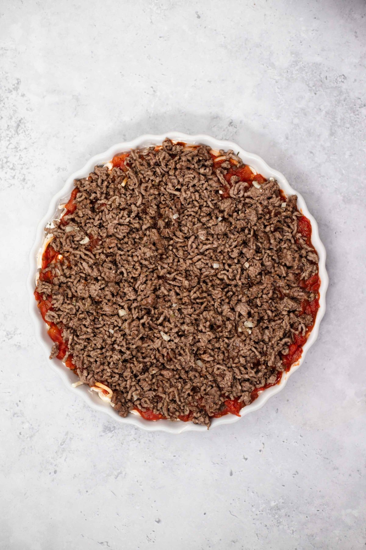 cheese, noodles, marinara, and beef in a circular baking dish