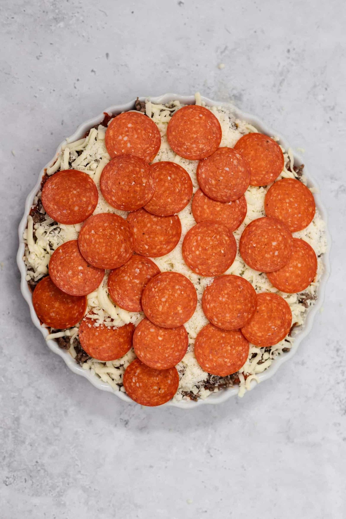 cheese, noodles, marinara, beef, cheese, and pepperonis in a circular baking dish
