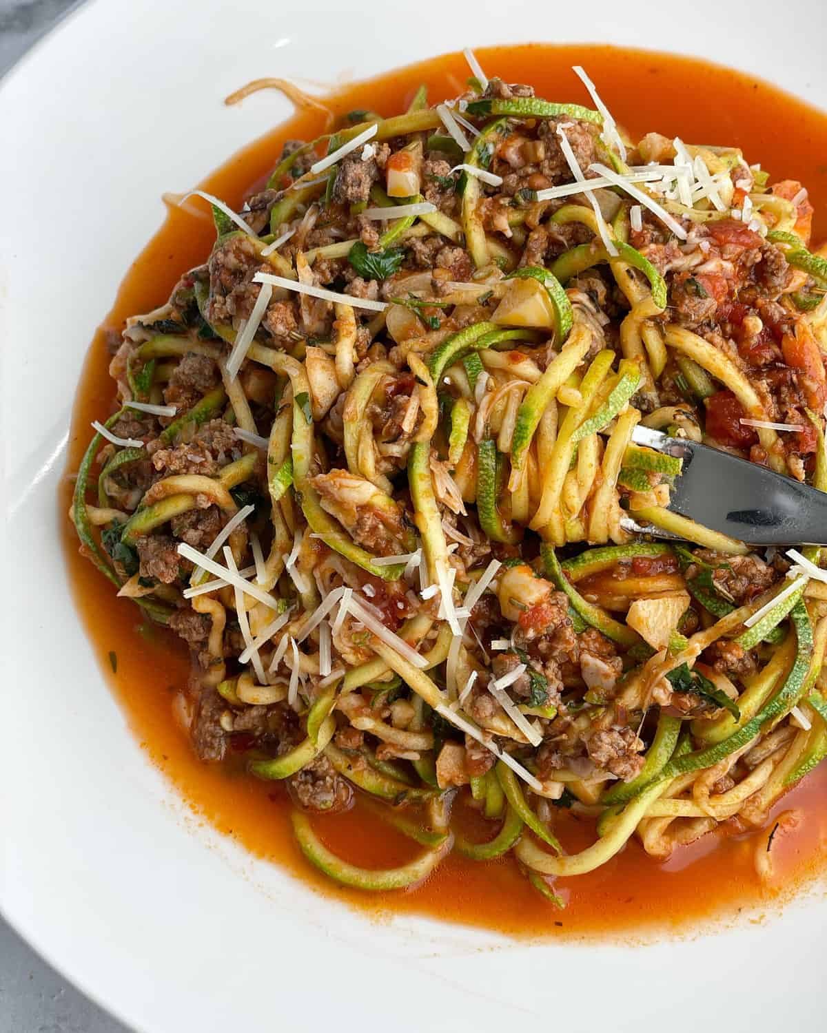 a bowl of low carb baked spaghetti zoodles with a bite being twirled around a fork