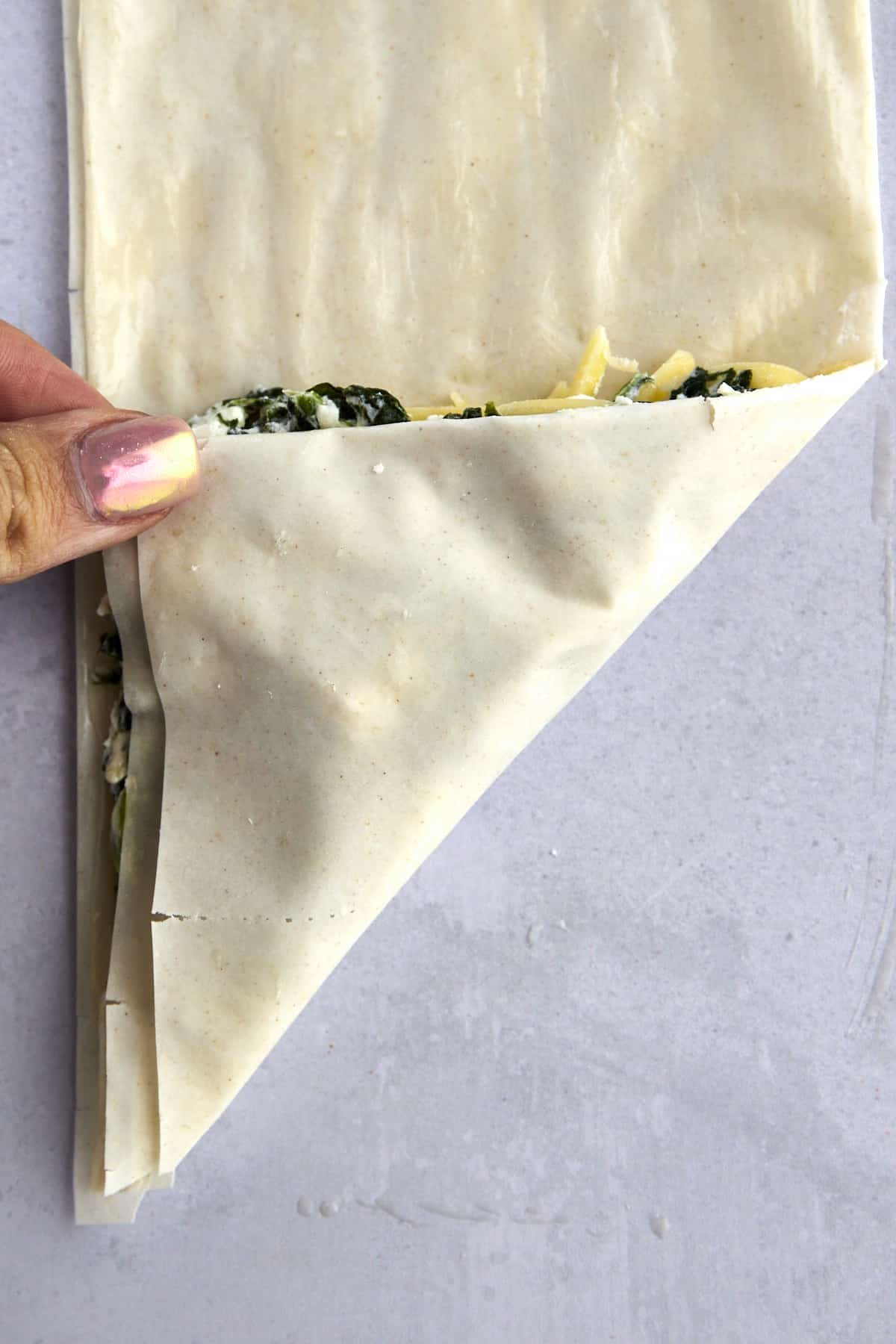 A hand folding phyllo dough over spanakopita filling.