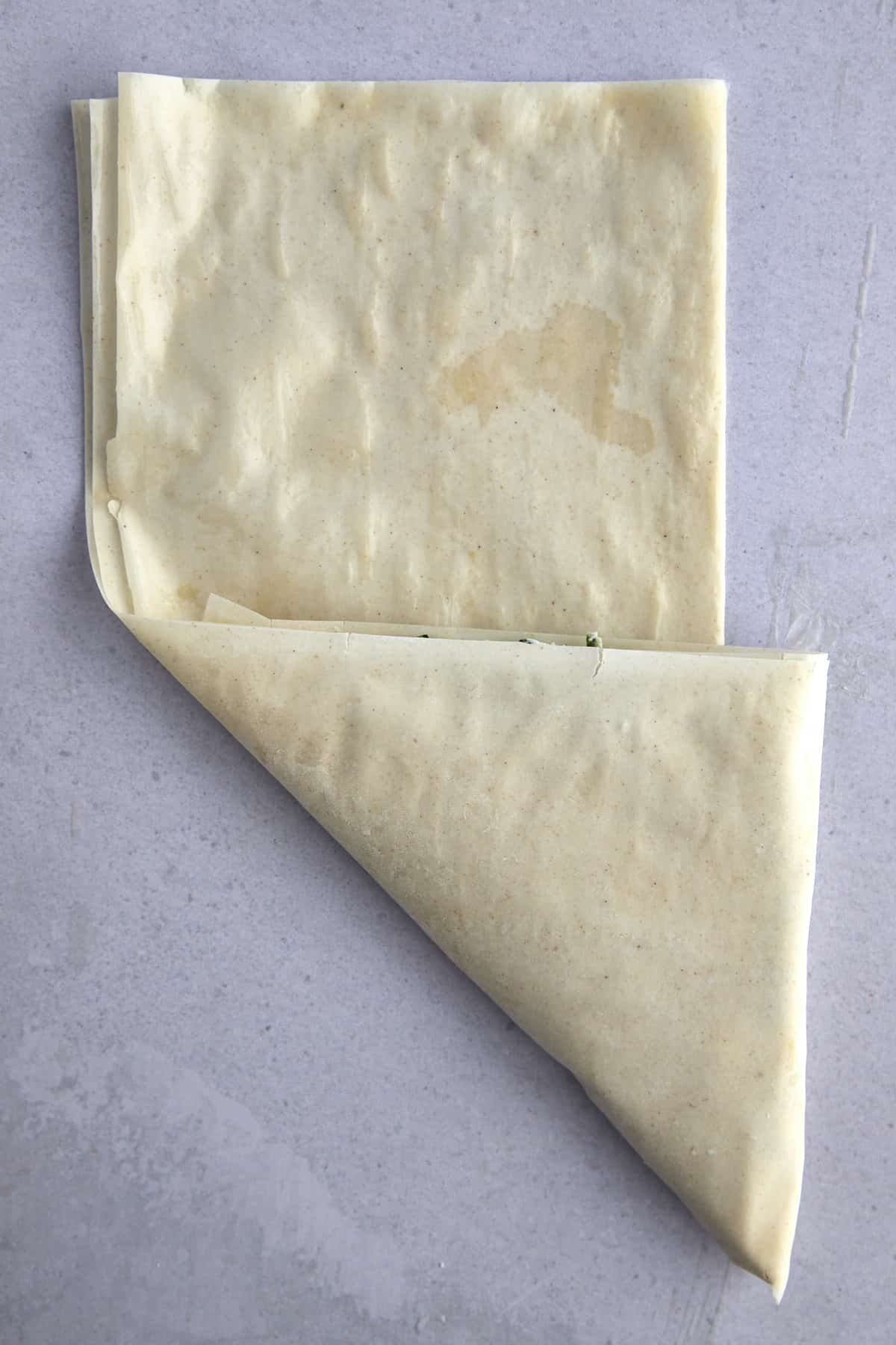 Raw phyllo dough being folded into a triangle.