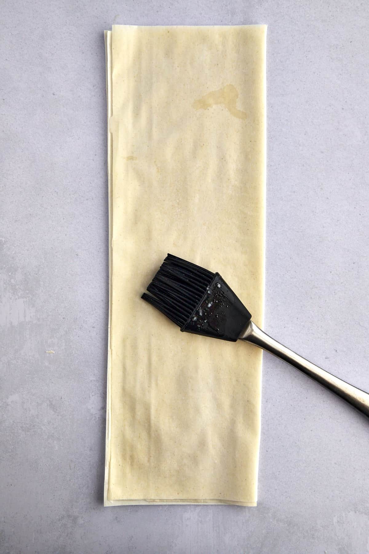 A pastry brush spreading dough over layered phyllo sheets.