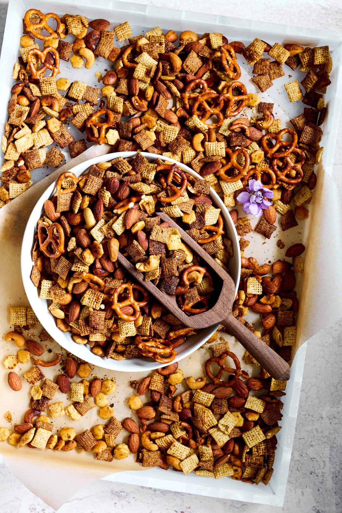 A bowl of spicy chex mix on top of a baking sheet of chex mix.