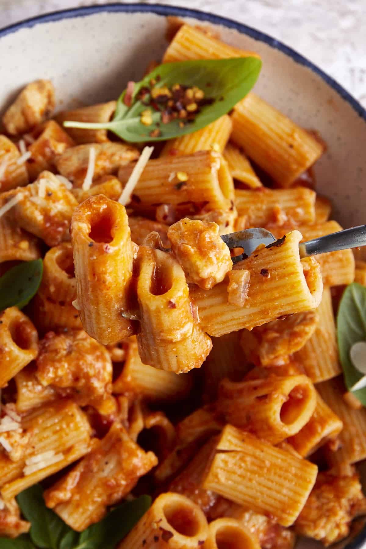 A fork holding a bite of spicy chicken rigatoni.