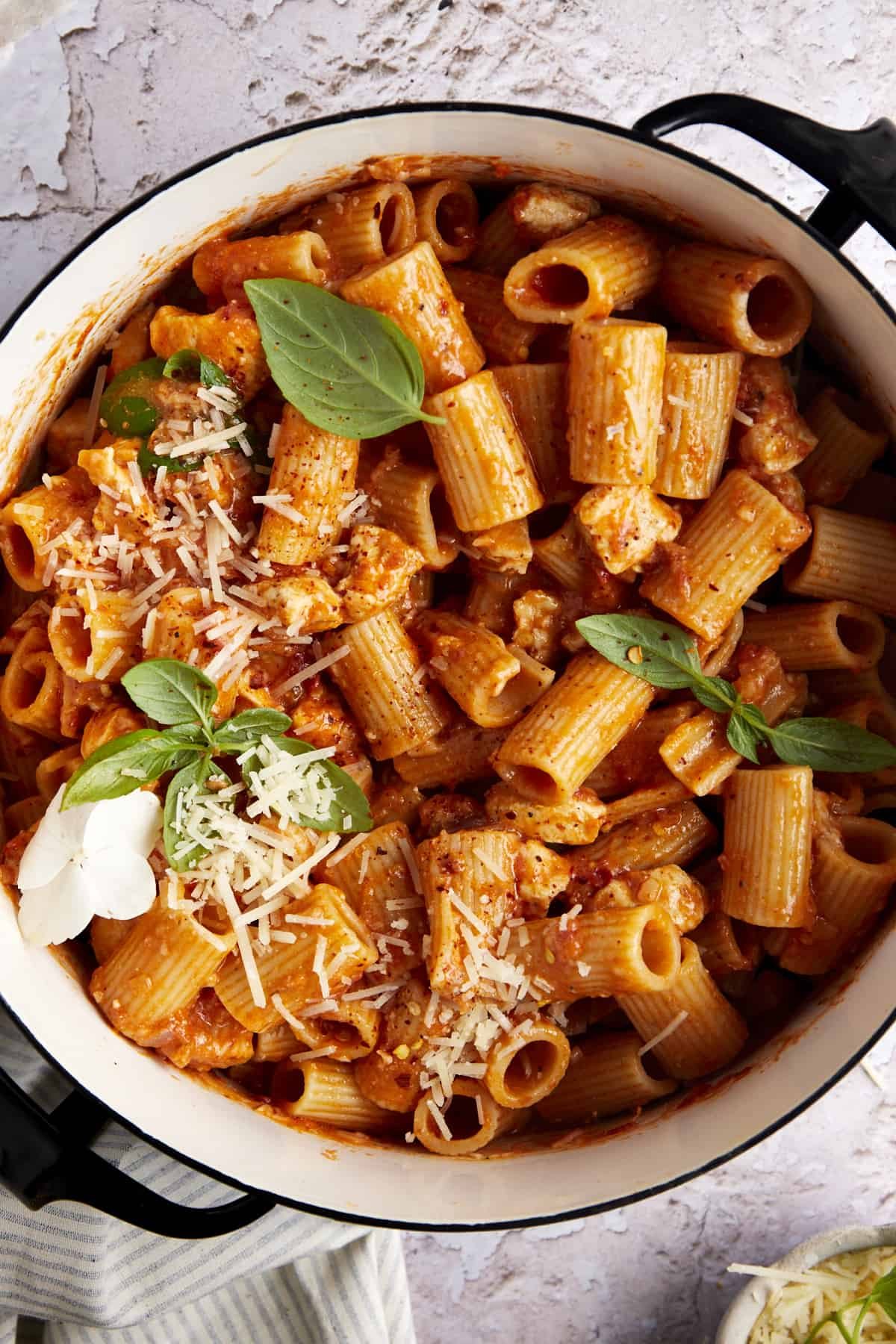 A pot full of spicy chicken rigatoni topped with fresh herbs and parmesan.
