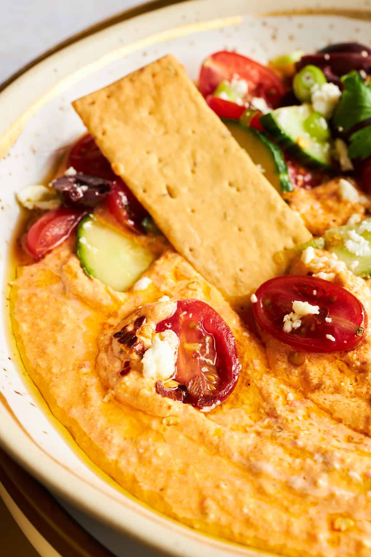 A cracker dipping into a bowl of spicy feta dip.