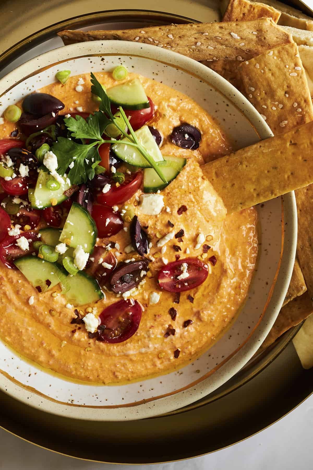 A bowl of spicy feta dip topped with veggies and olives.