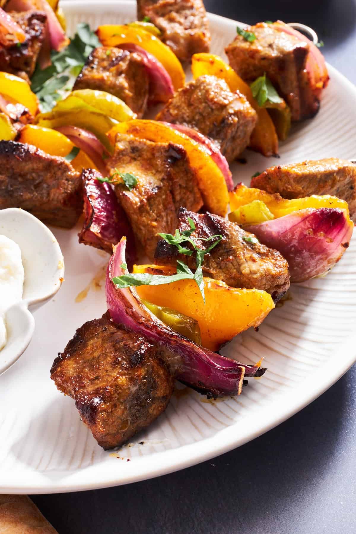 Close up of grilled steak skewers with onions and peppers on a plate.