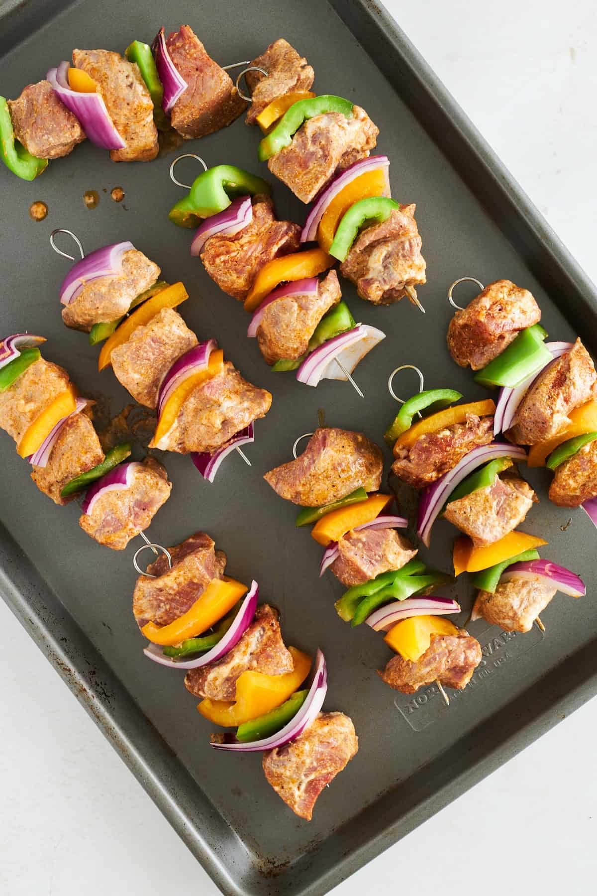 Raw steak skewers on a baking sheet.