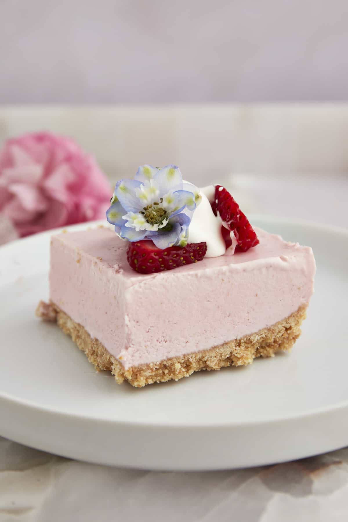 A no-bake strawberry cheesecake square on a plate topped with strawberries and whipped cream.