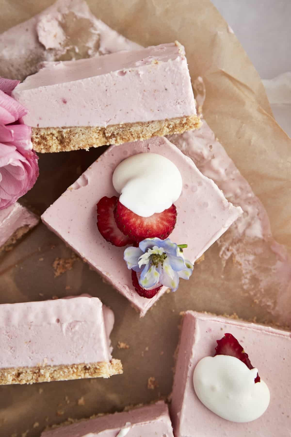 Overhead image of strawberry cheesecake squares on parchment paper.