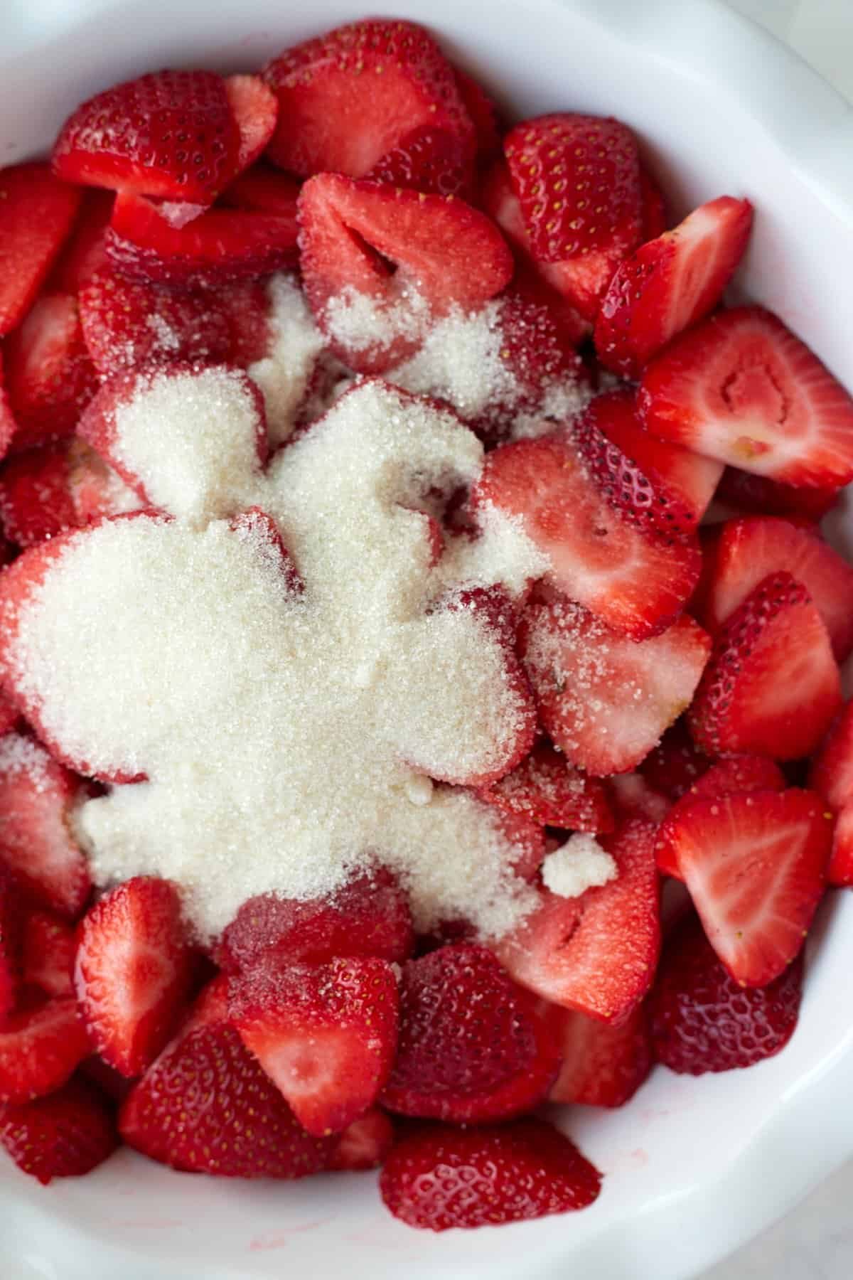 A bowl of fresh strawberries topped with sugar.