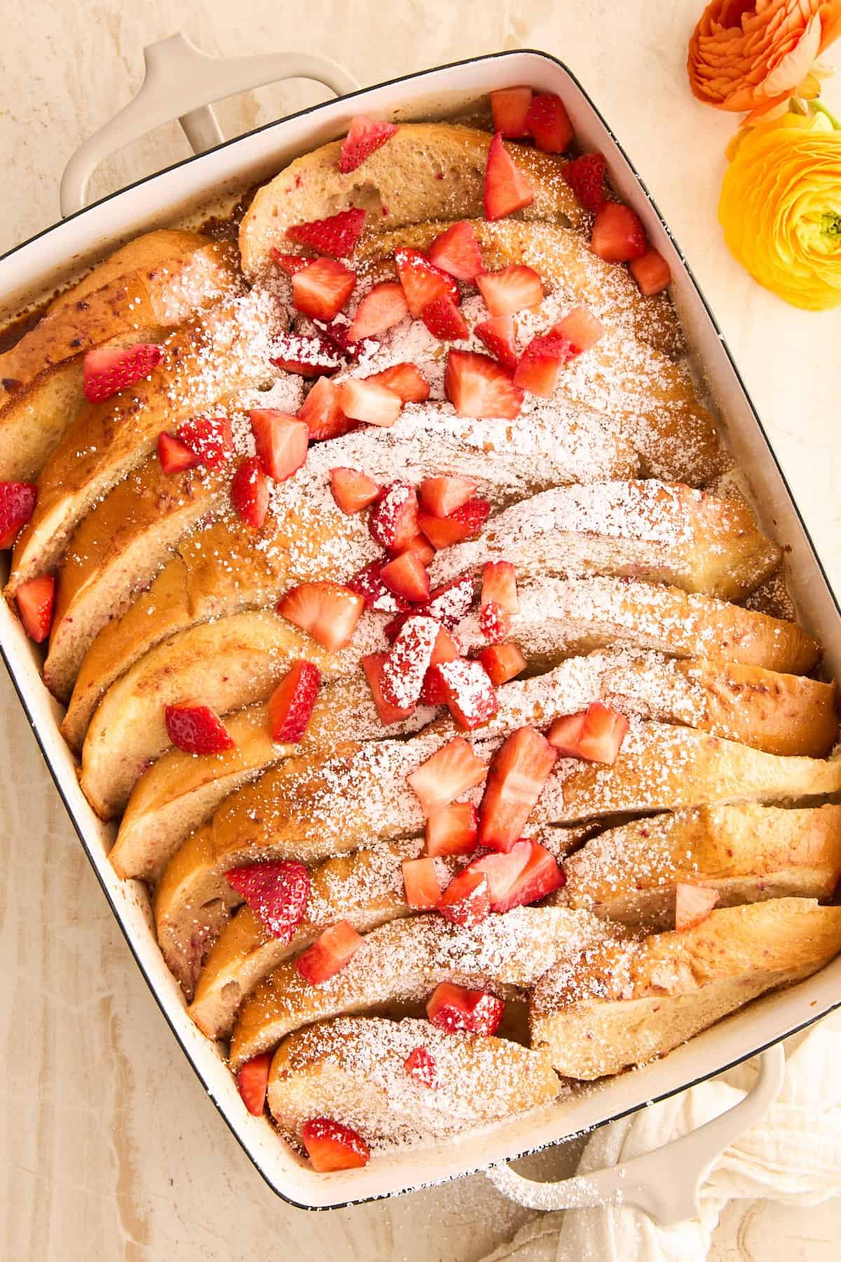 A baking dish full of whole pieces of strawberry french toast topped with powdered sugar and strawberries.