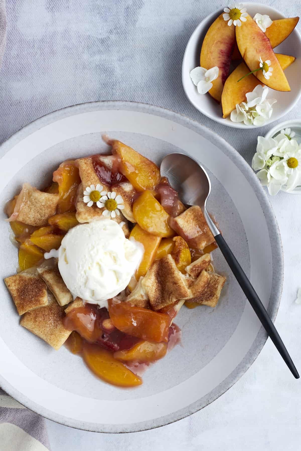 a bowl of simple peach strawberry cobbler topped with vanilla ice cream with a small bowl of peaches on the side