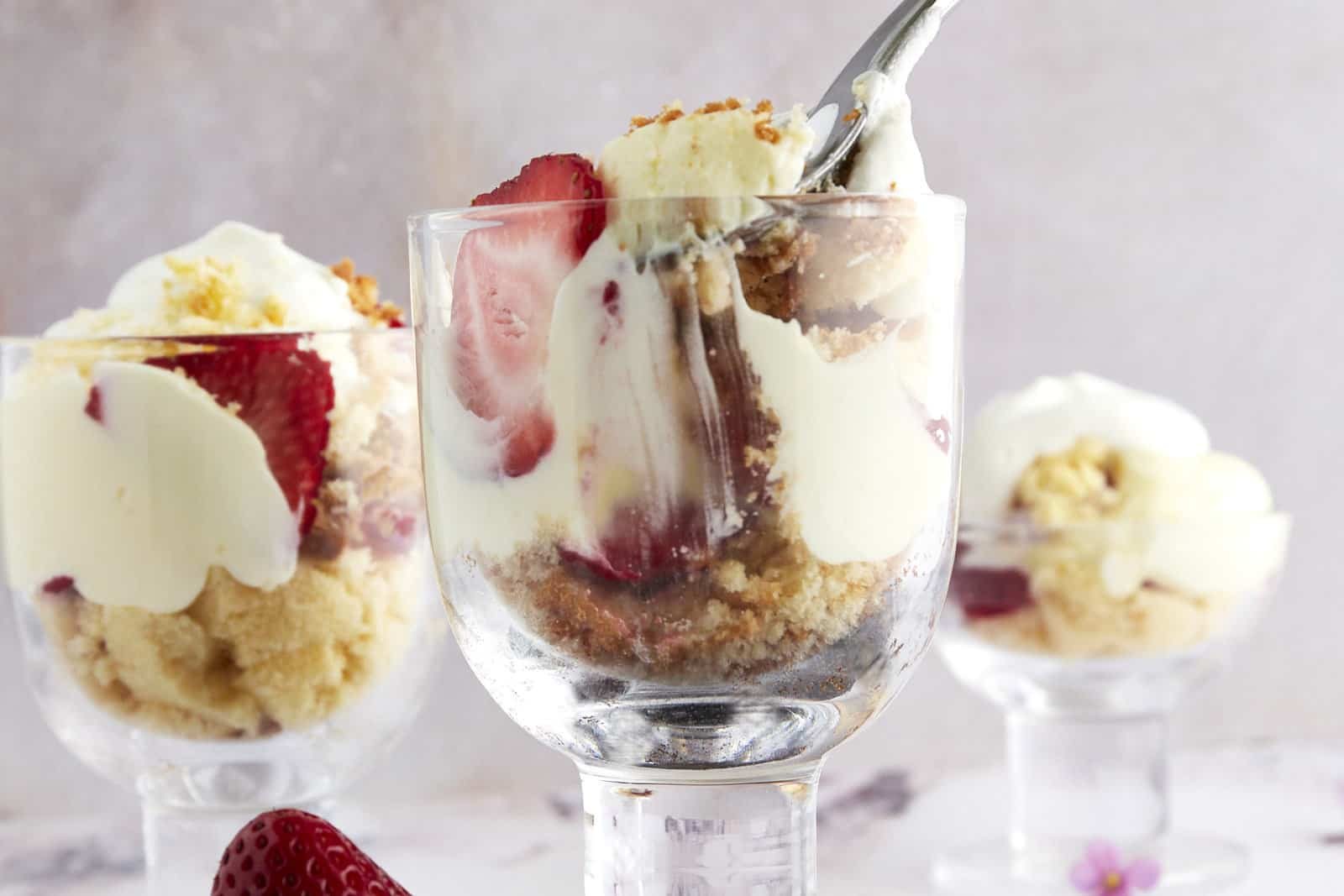 Three glasses full of strawberry shortcake with a fork pulling a bite from one.