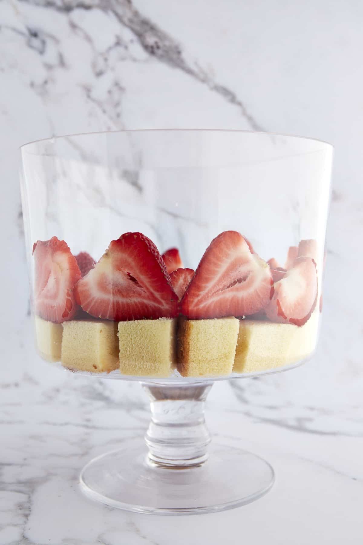 A trifle bowl with a layer of pound cake cubes topped with strawberries.