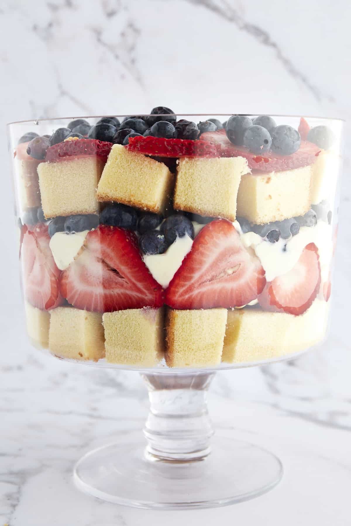 A trifle bowl full of layers of pound cake, strawberries, whipped topping, and blueberries.