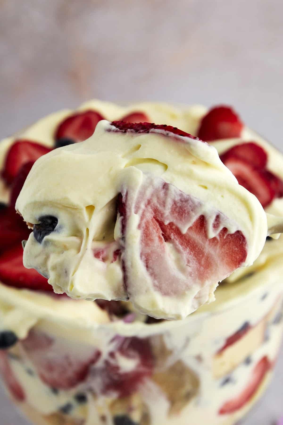 A spoonful of summer berry trifle with strawberries and blueberries.