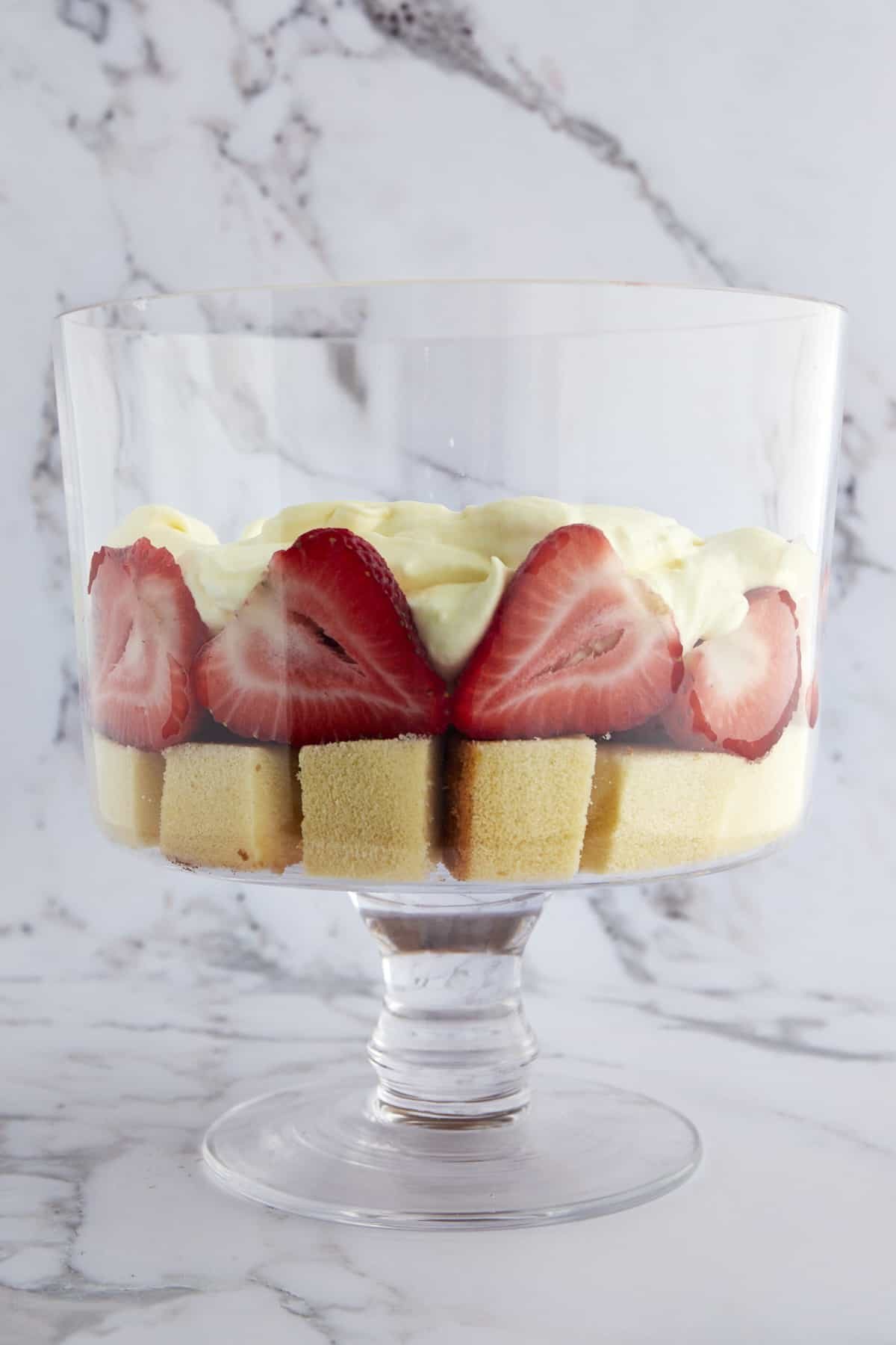 A trifle bowl with a layer of pound cake, strawberries, and whipped topping.