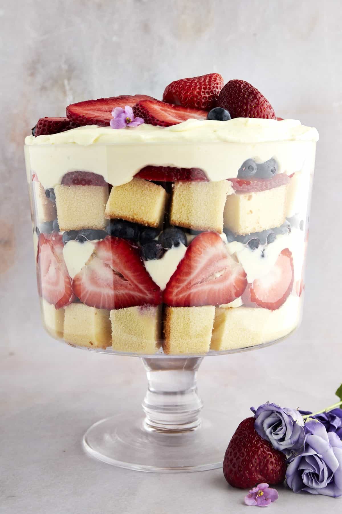 Side view of a trifle bowl full of pound cake, strawberries, whipped topping, and blueberries.