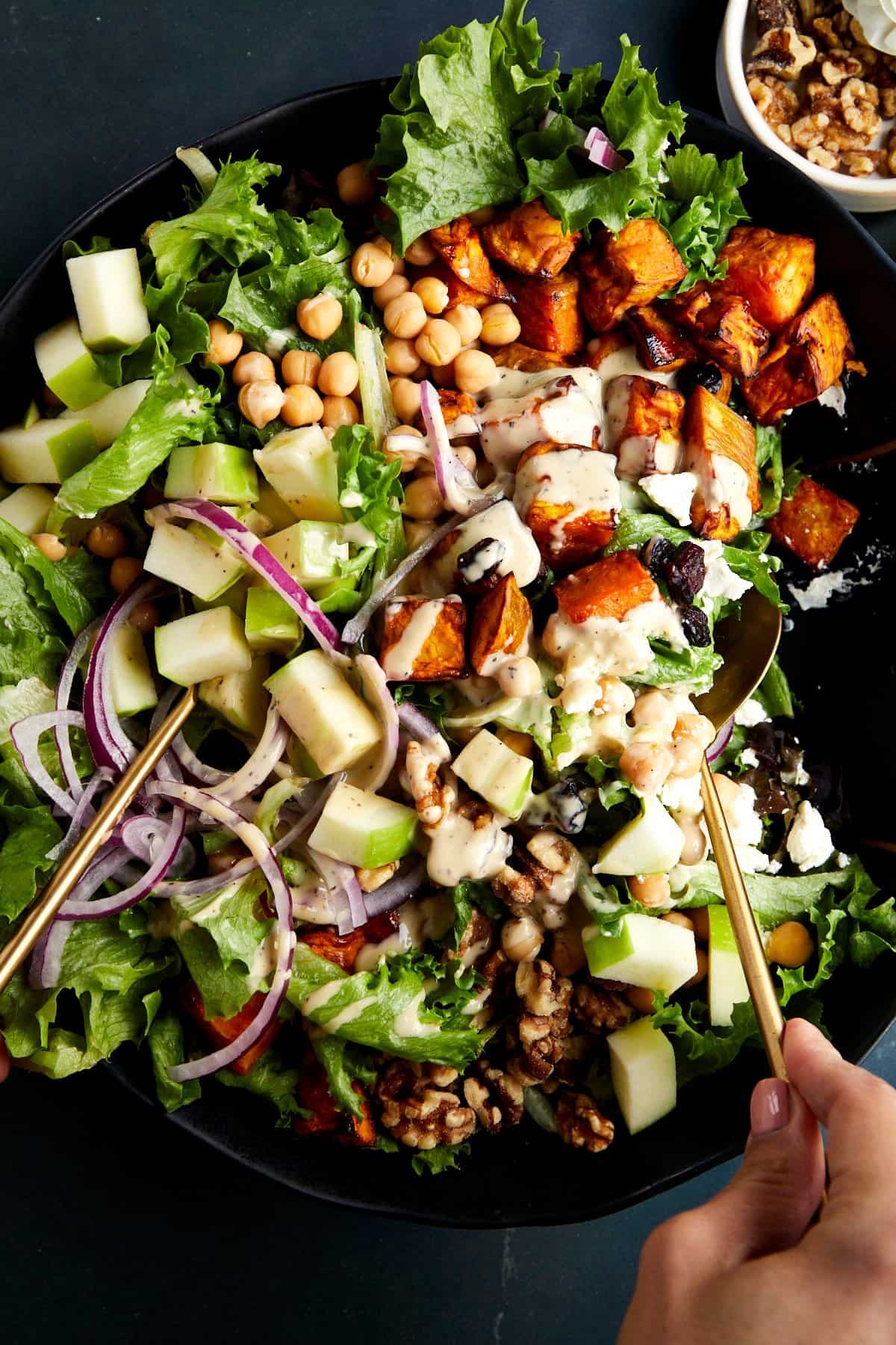 A sweet potato salad with chickpeas being tossed with tahini dressing.