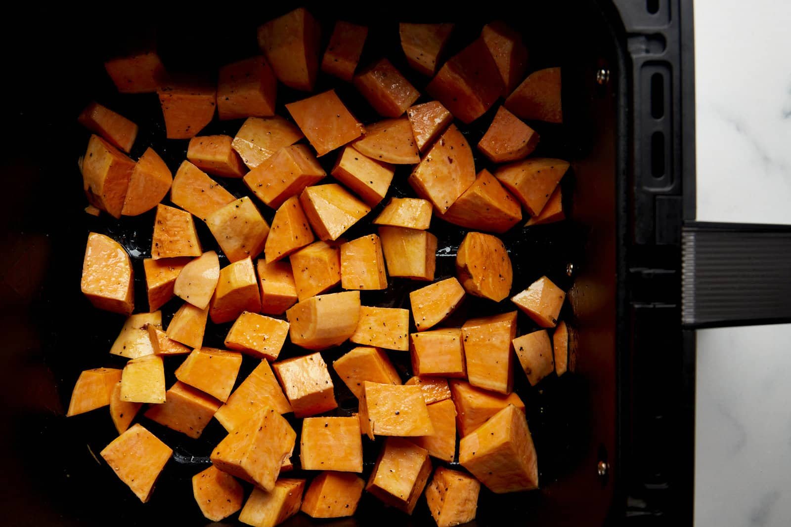 Raw sweet potato cubes in an air fryer basket.