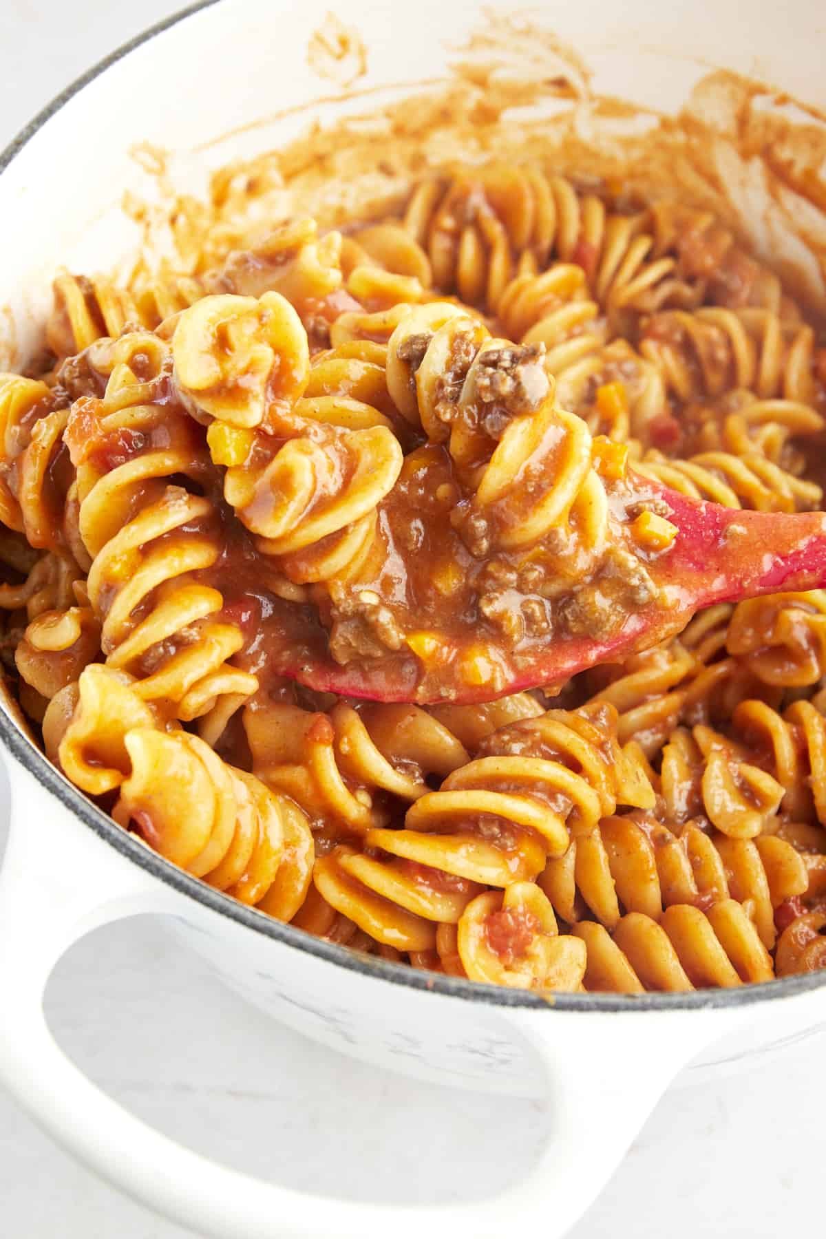 A rubber spoon stirring cooked taco pasta in a pot.
