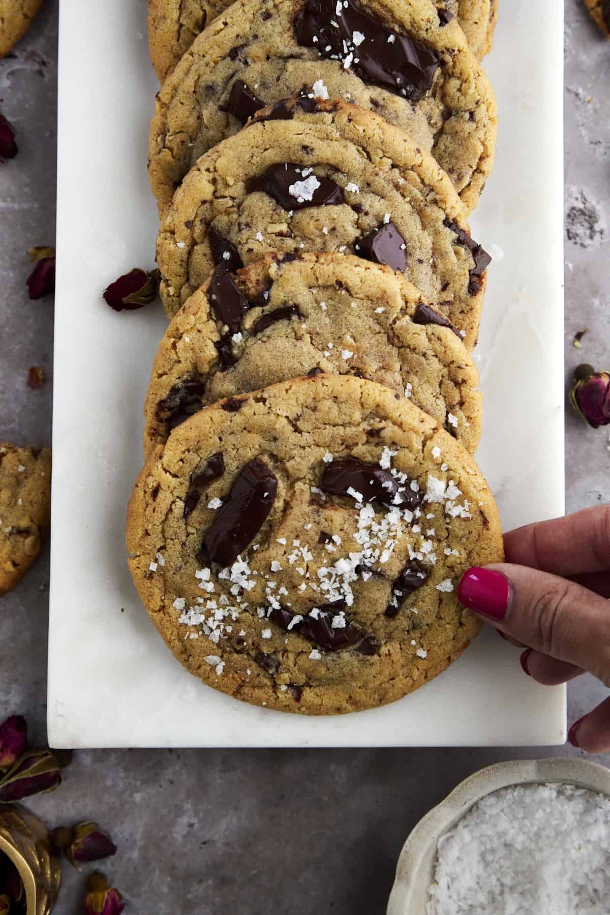 a hand grabbing a cookie from a plate full of tahini chocolate chip cookies arranged in a row
