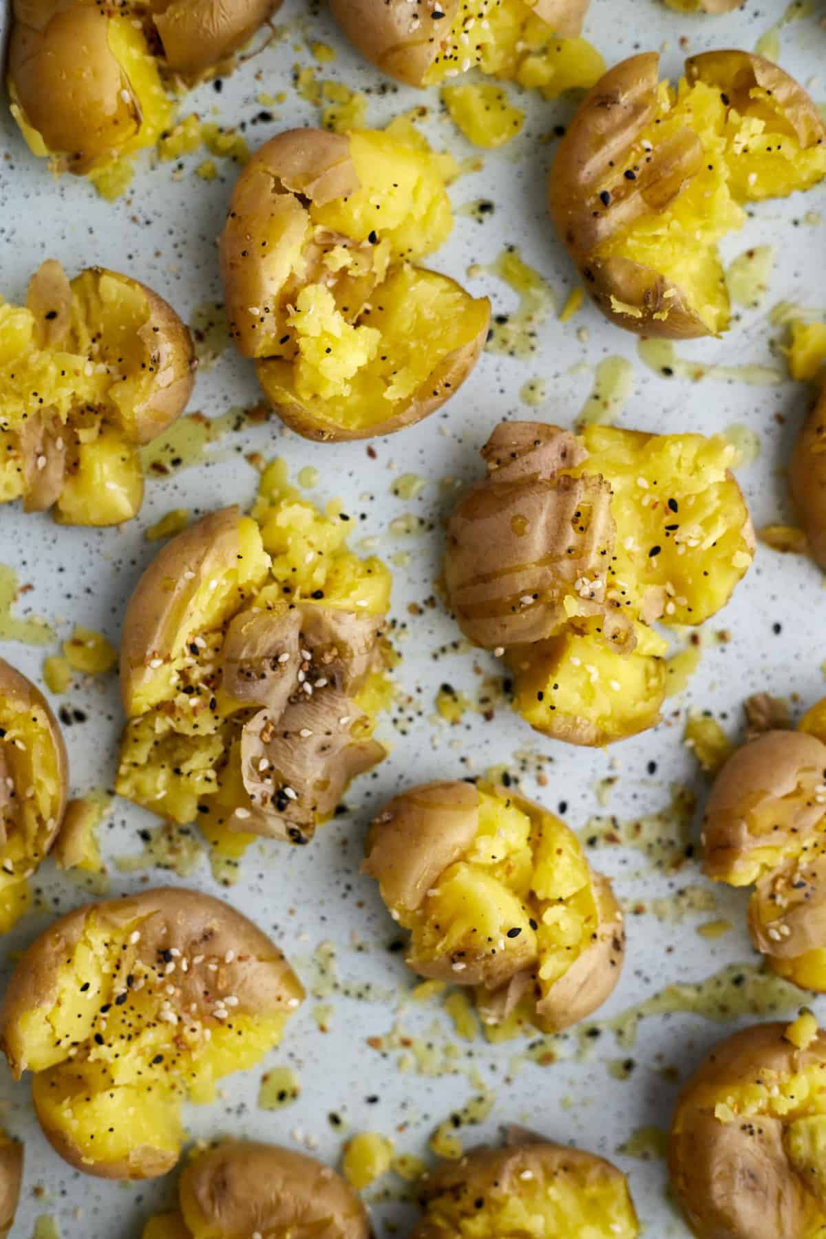 Boiled smashed potatoes on a baking sheet topped with everything but the bagel seasoning.