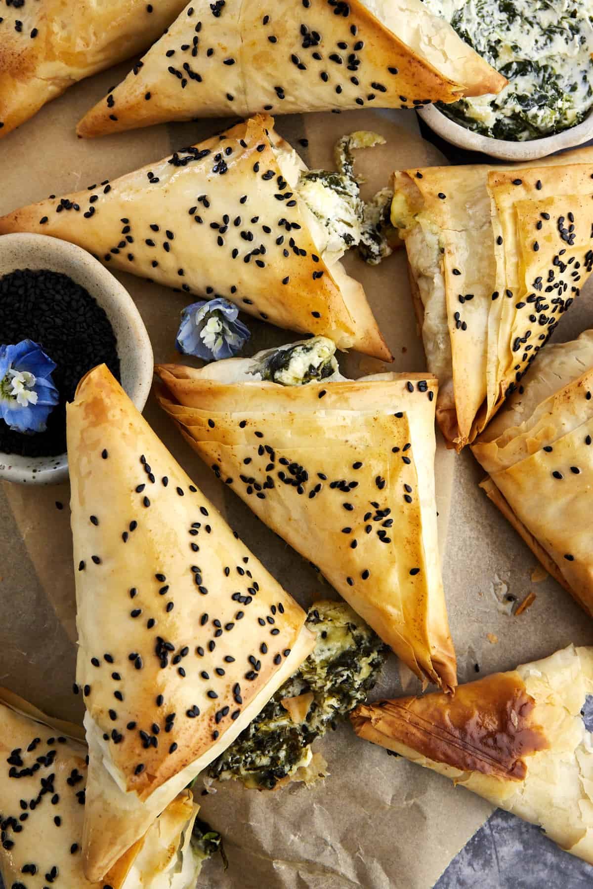 Baked spanakopita triangles topped with black sesame seeds on parchment paper.