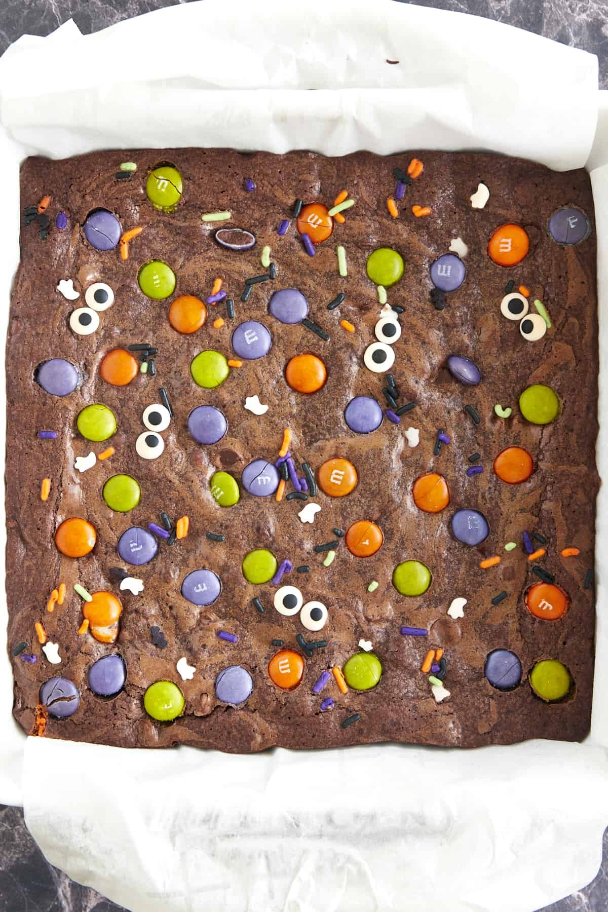 A baking dish full of Halloween brownies topped with M&Ms, sprinkles, and candy eyes.