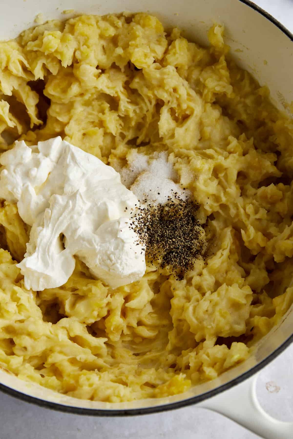 Sour cream and seasonings on top of mashed potatoes in a pot.