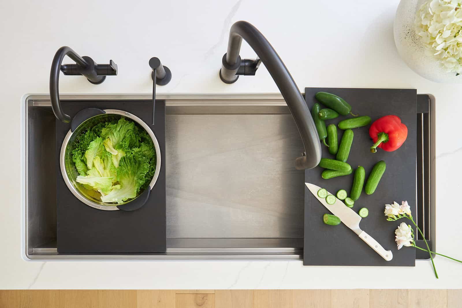Overhead image of a clean kitchen sink with a colander attachment and a cutting board attachment.