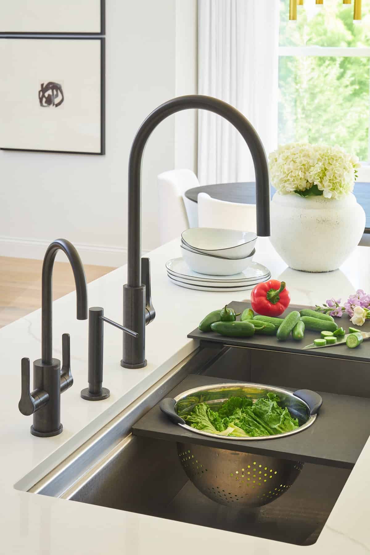 A kitchen sink with attachments for a cutting board with veggies and a colander.