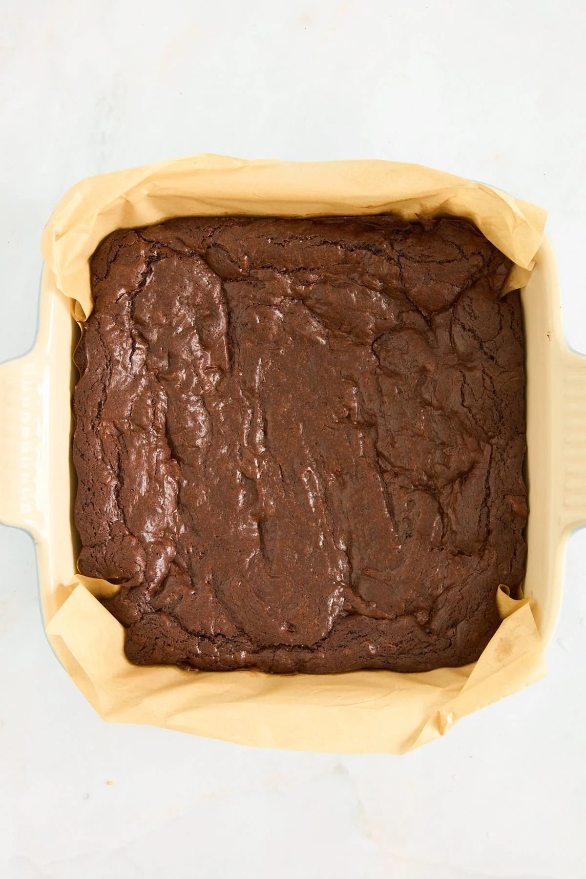 Baked brownies in a parchment paper lined baking dish.