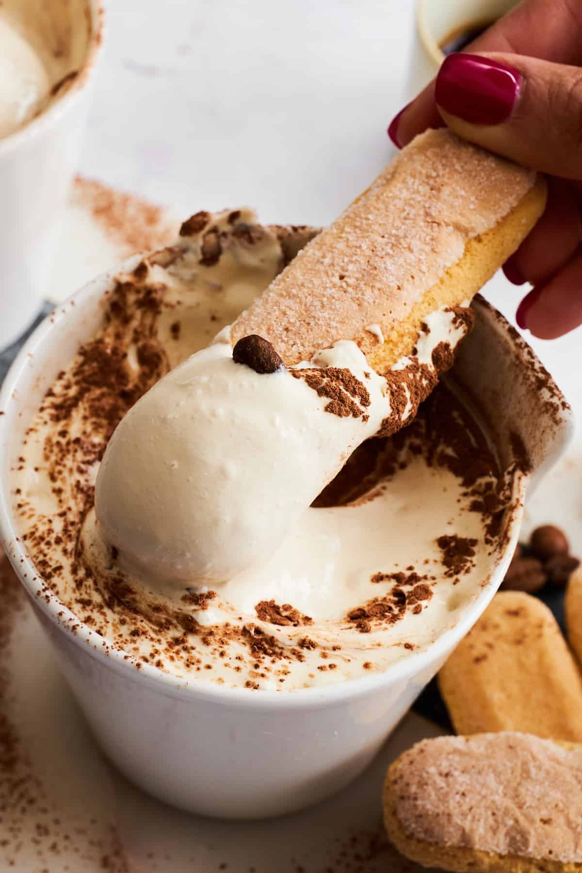 A ladyfinger cookie being dipped into a bowl of tiramisu dip.