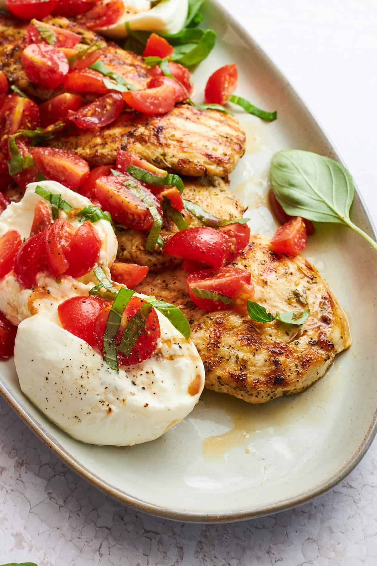 A plate of tomato basil chicken with balls of burrata.