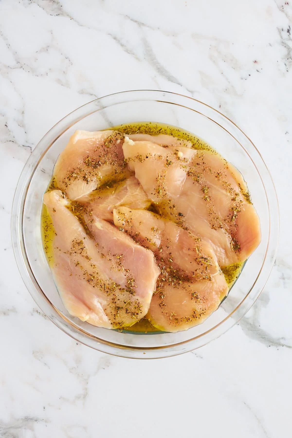 A bowl of chicken breasts in an olive oil marinade.