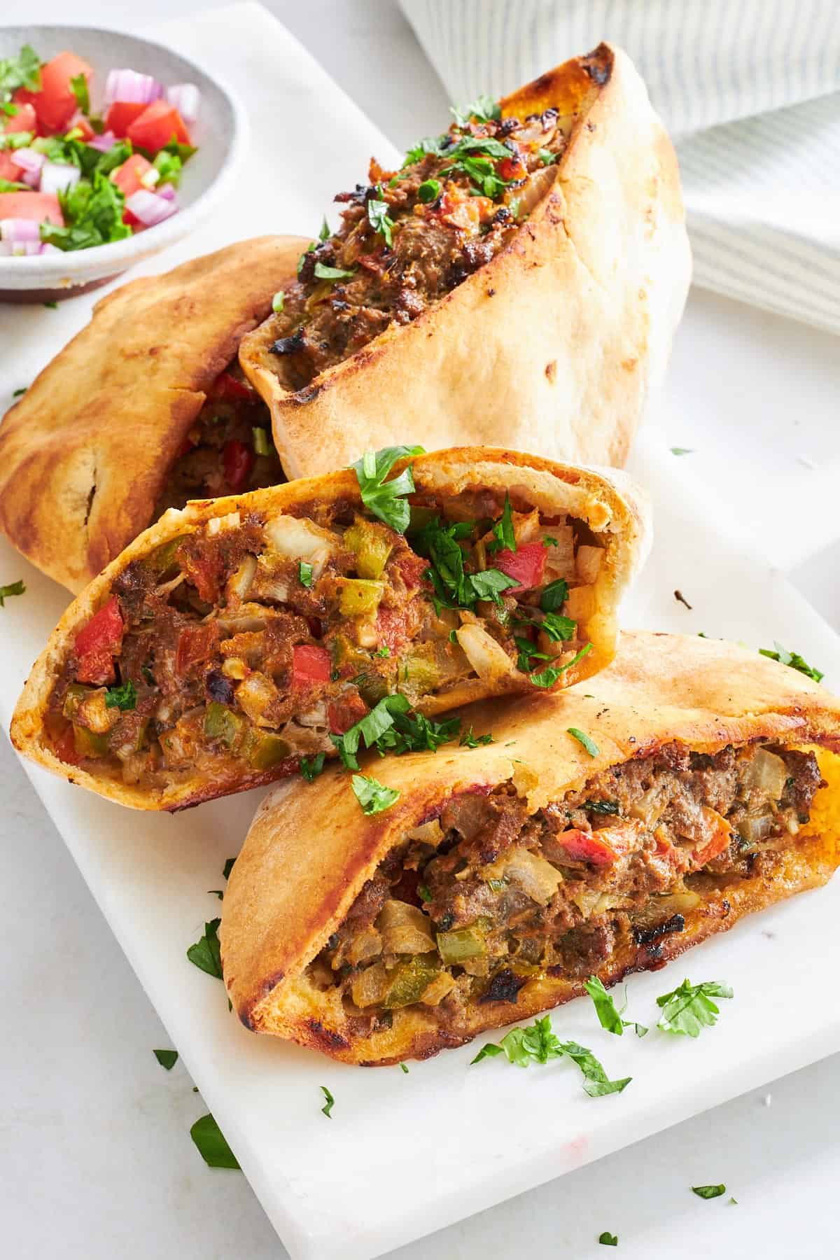 Four baked veggie-packed hawawshi pita halves on a plate.