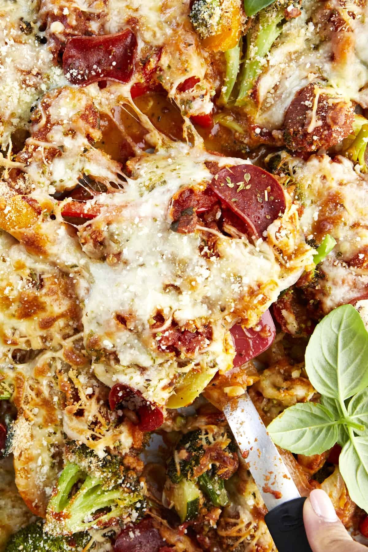 A portion of veggie pizza being lifted from a baking sheet.
